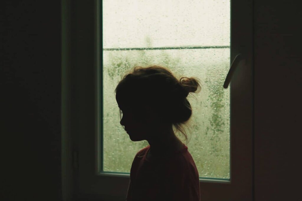 Silueta de una persona frente a una ventana que representa el impacto de los traumas infantiles en la edad adulta.