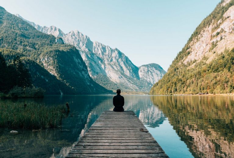 meditacion-mindufulness-hugo-filippe Imágen de hombre sentado de espaldas, contemplando un bello paisaje con montaña y lago, representado la meditación budista y mindfulness que aplica Hugo Filippe en su psicoterapia